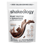 A stand-up pouch of Shakeology Plant Protein + Superfoods in chocolate flavor, shown on a plain white background. The packaging is white with black text and a large chocolate splash graphic on the front, plus callout icons for protein, added sugar, calories, and fiber.